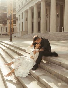 a man and woman sitting on steps in front of a building, kissing each other