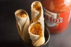 two burritos are sitting in a bowl next to a can of hot sauce