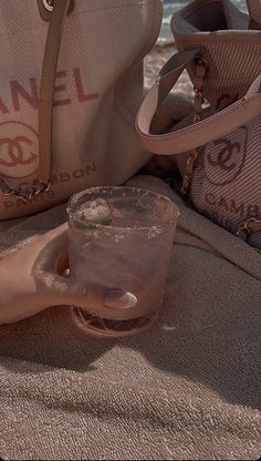 a person holding a drink in their hand while sitting on the beach with other purses