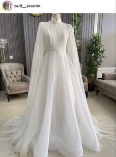 a white wedding dress with long sleeves and a train on display in front of a chair