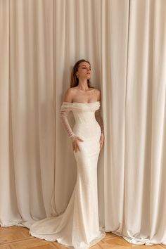 a woman standing in front of a curtain wearing a white dress