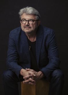 an older man with glasses is sitting on a wooden stool and looking at the camera