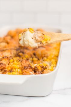 a spoon full of food with corn on the cob and meat in it is being lifted from a casserole dish