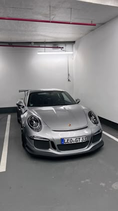 a silver sports car parked in a parking garage next to a white wall and ceiling