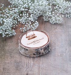 a wooden ring box sitting on top of a piece of wood next to white flowers