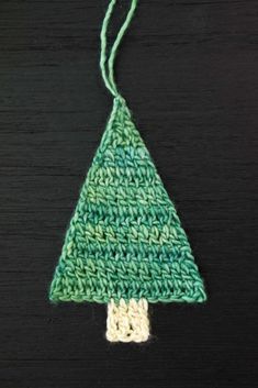 a crocheted christmas tree ornament hanging on a wooden table with green yarn