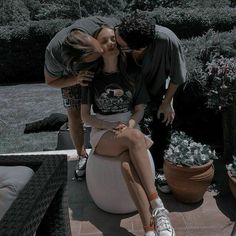 two people are kissing while sitting on a toilet in the middle of a yard with potted plants