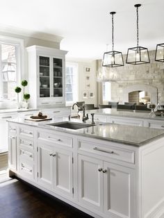 a large kitchen with white cabinets and marble counter tops, an island style sink and oven