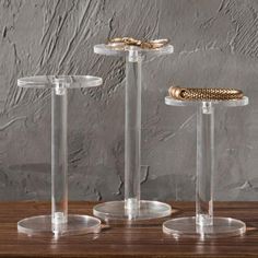 three clear acrylic pedestals with gold rings on them, one is empty