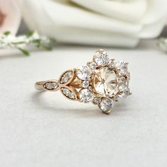 a close up of a ring on a table with flowers in the background and a white rose behind it