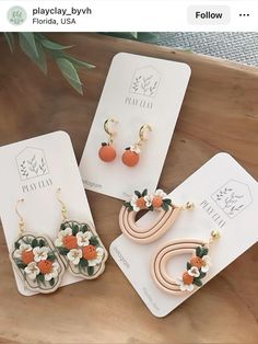 three pairs of earrings with flowers on them sitting on top of a wooden table next to each other