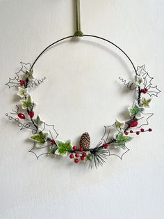 a christmas wreath with holly, pineconis and berries hanging from a hook on the wall