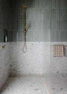 a bathroom with green and white tiles on the walls, shower head and hand held faucet