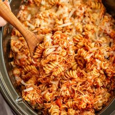 the pasta is being cooked in the crock pot with a wooden spoon to stir it