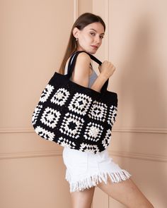 a woman carrying a black and white crocheted bag with fringes on it