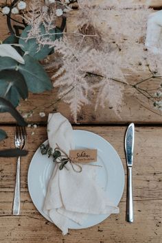 a place setting with napkins and silverware on a wooden table next to flowers