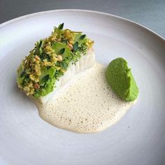 a white plate topped with a piece of fish next to a green substance on top of it