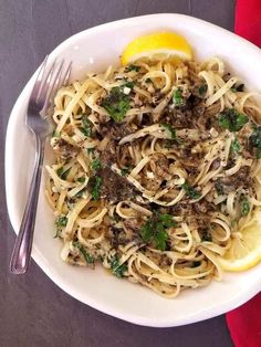 a white plate topped with pasta and meat next to a lemon wedge on a table