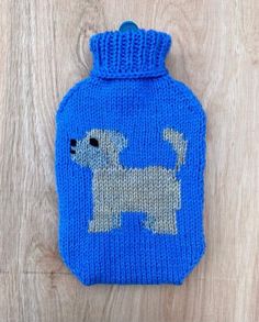 a blue knitted hot water bottle with a dog on it's side sitting on a wooden surface