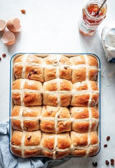 hot cross buns in a blue baking dish on a white table with eggs and butter