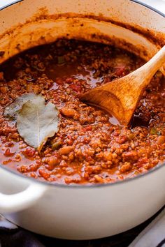 a wooden spoon in a white pot filled with chili and ground beef sauce on top of a table