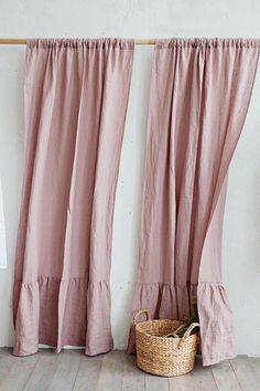 a basket sitting on the floor in front of two pink curtains with ruffled edges