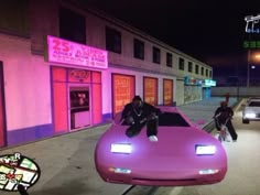 a man sitting on top of a purple car in front of a pink building at night