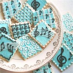 decorated cookies with music notes and trebles are on a white plate next to blue icing