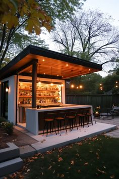 an outdoor bar with stools and lights in the back yard at dusk, surrounded by trees