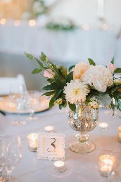 a vase filled with white flowers sitting on top of a table next to lit candles