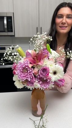 a woman is holding a vase with flowers in it on a counter top next to a microwave