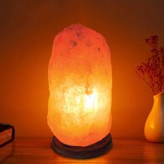 a himalayan salt lamp sitting on top of a wooden table next to a vase with flowers