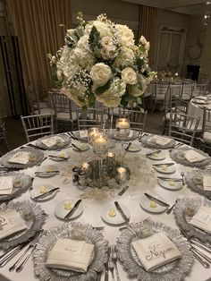 the centerpiece is surrounded by silver and white plates, napkins, and candles