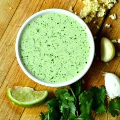 a bowl filled with green liquid surrounded by cilantro and garlic