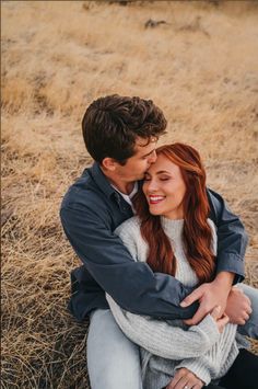 a man and woman sitting on the ground hugging each other in front of dry grass