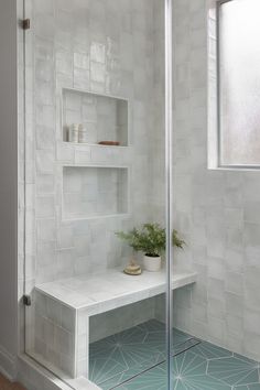 a white tiled bathroom with shelves and plants on the shelf next to the shower door