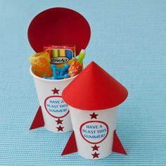 two paper cups with candy in them on a blue tableclothed surface, one is red and the other is white