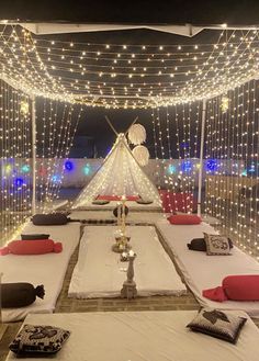 an outdoor tent with lights and pillows on the floor, set up for a party