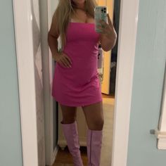 a woman in a pink dress taking a selfie with her cell phone while wearing knee high boots