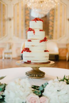 a white wedding cake with red berries on top sits on a table surrounded by flowers