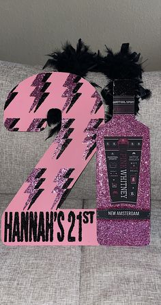 a pink and black number two sign sitting on top of a couch next to a bottle of booze