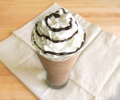 a cup with whipped cream and chocolate swirl on it sitting on a napkin next to a fork