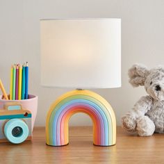 a white teddy bear sitting next to a lamp on a table with a rainbow decoration