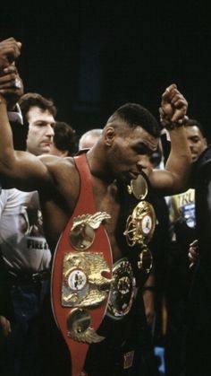 the professional boxer is holding his belt in front of other people as he stands next to him