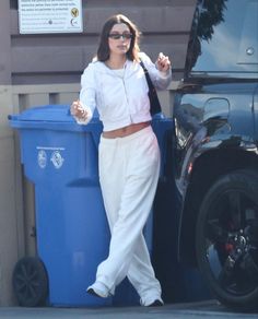 a woman in white is standing next to a blue trash can and holding her hand out