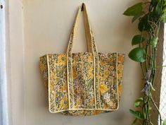 a yellow floral bag hanging on a wall next to a plant and potted plant