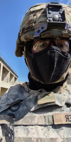 a soldier wearing a face mask and holding a camera in his hand with the sky behind him