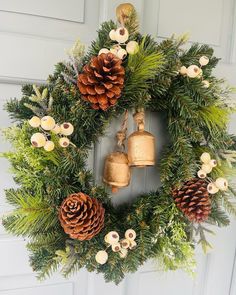 a wreath with pine cones and bells hanging from the front door, decorated with greenery