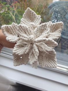 a hand holding up a knitted snowflake in front of a window