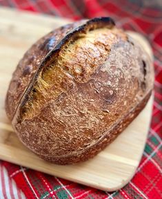 a loaf of bread sitting on top of a wooden cutting board next to a red and green checkered table cloth